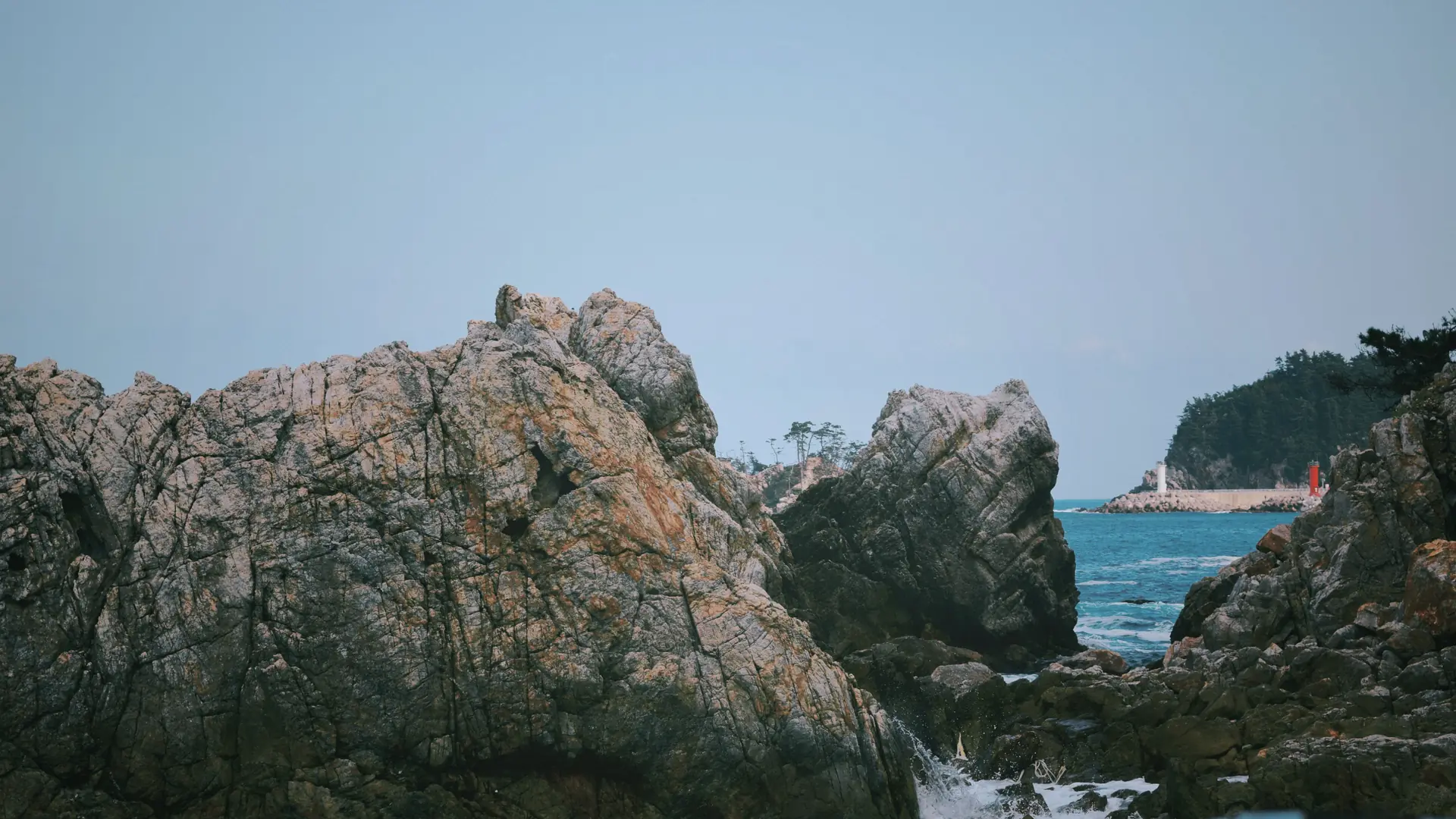 Yongduam Dragon Head Rock's jagged volcanic silhouette against a clear blue sky and sea, with a lighthouse visible behind it, Jeju City