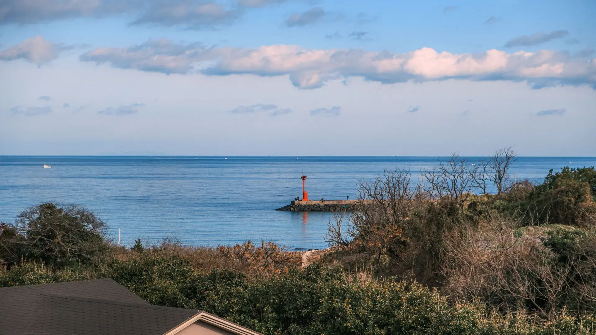 A coastal lighthouse and breakwater on Jeju's coastline in bright daylight