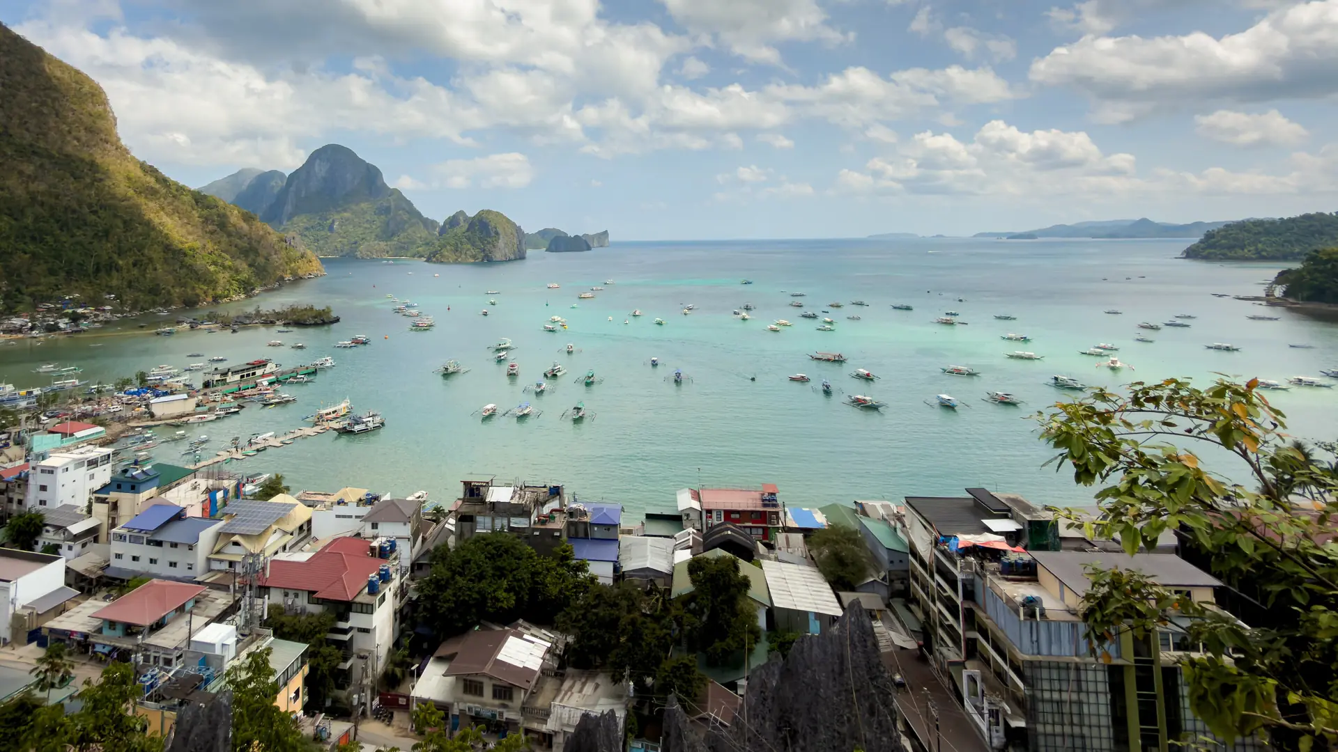 Aerial view of El Nido Town Beach, its rooftops and moored bancas on Bacuit Bay beneath limestone hills