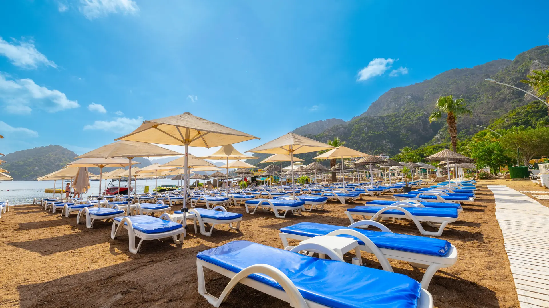 Blue sunbeds, pale parasols and mountain slopes beside sunny İçmeler beach