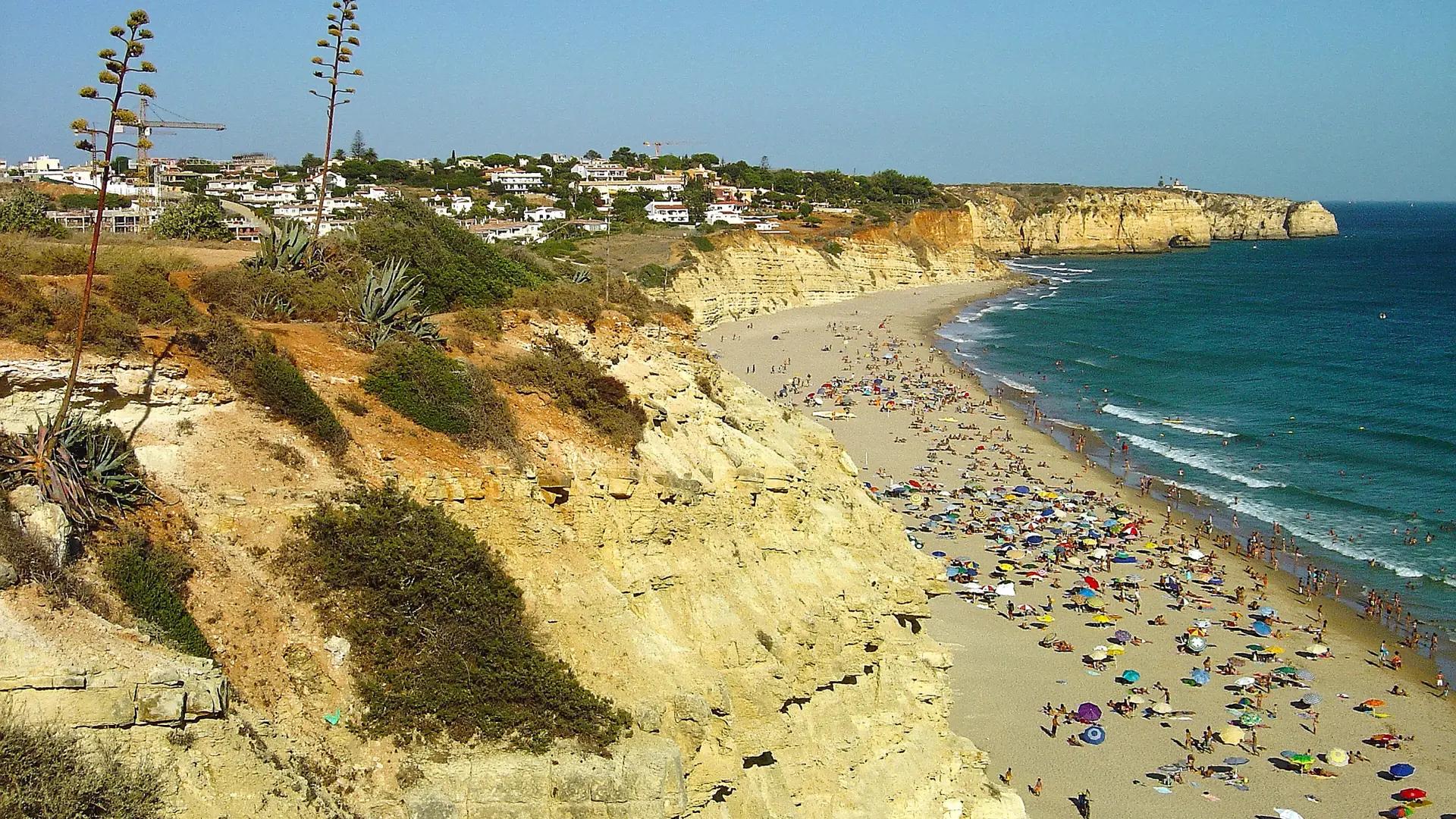 Beachgoers on Porto de Mós sand below pale layered cliffs beside the blue Atlantic