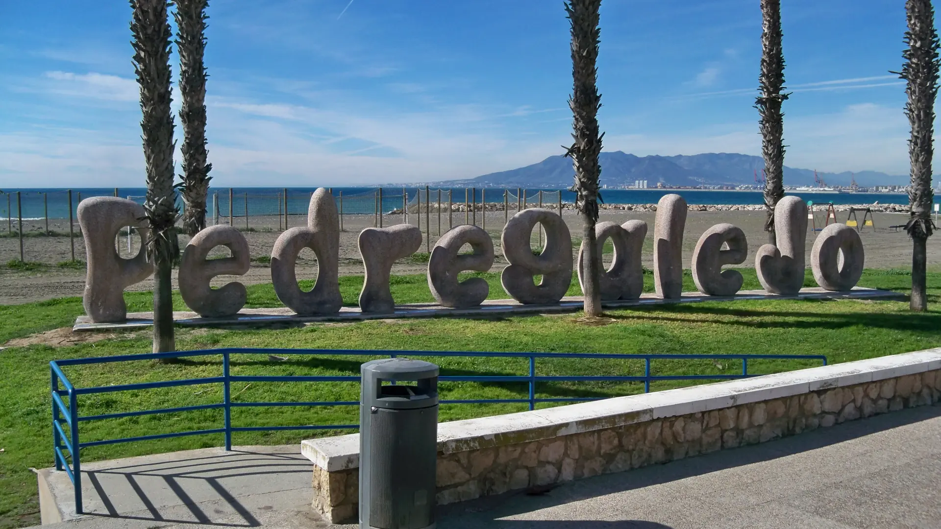 Pedregalejo beach sign between palm trees with the sea behind it