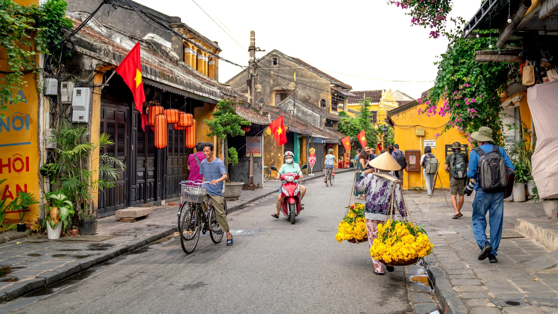 Flags and lanterns above a bright historic street in Hoi An