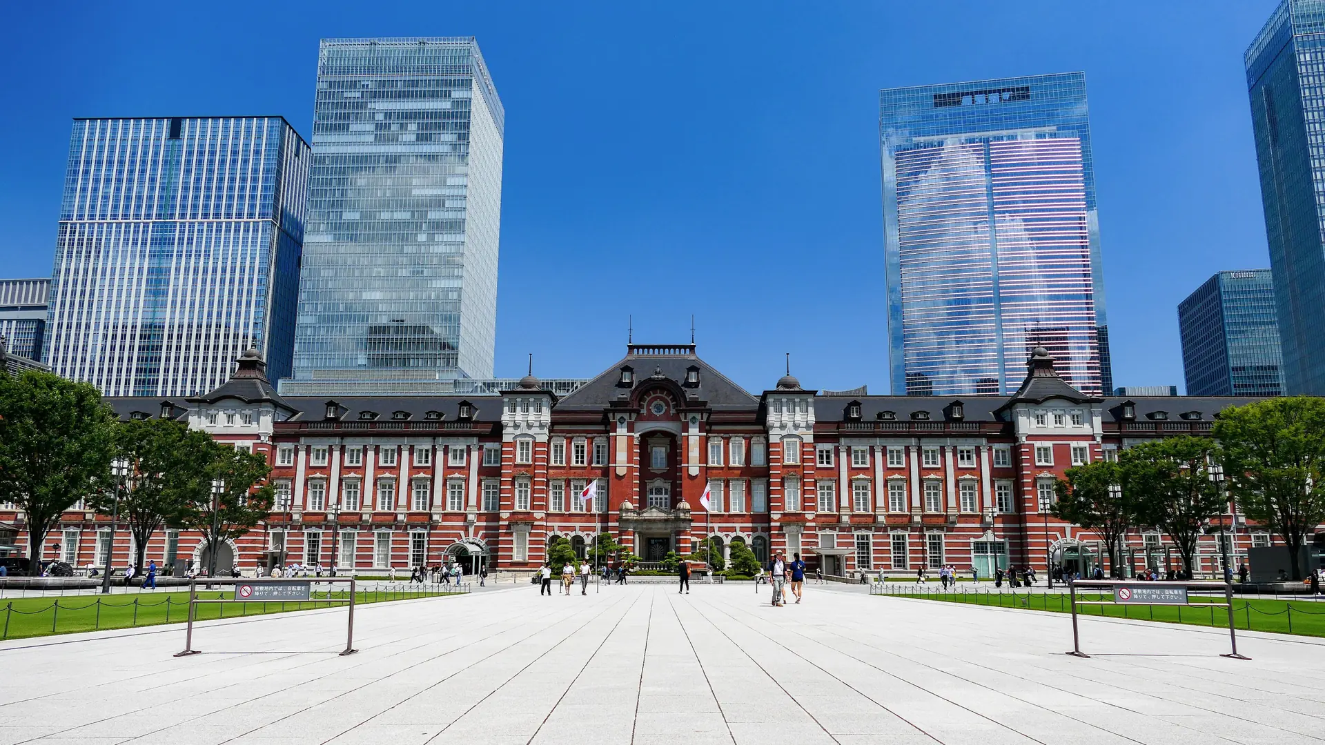 Tokyo Station's red-brick Marunouchi facade framed by sunlit modern skyscrapers
