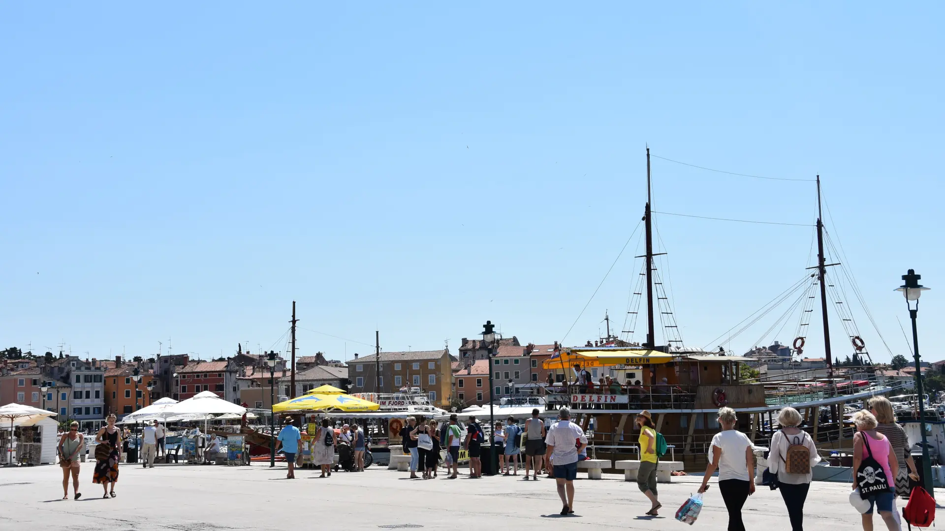 Rovinj harbour waterfront with excursion boats, colourful buildings and people walking