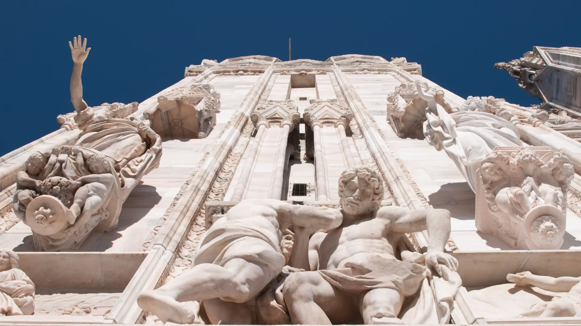 detailed marble sculptures on the Duomo's facade against a vivid blue sky in Milan