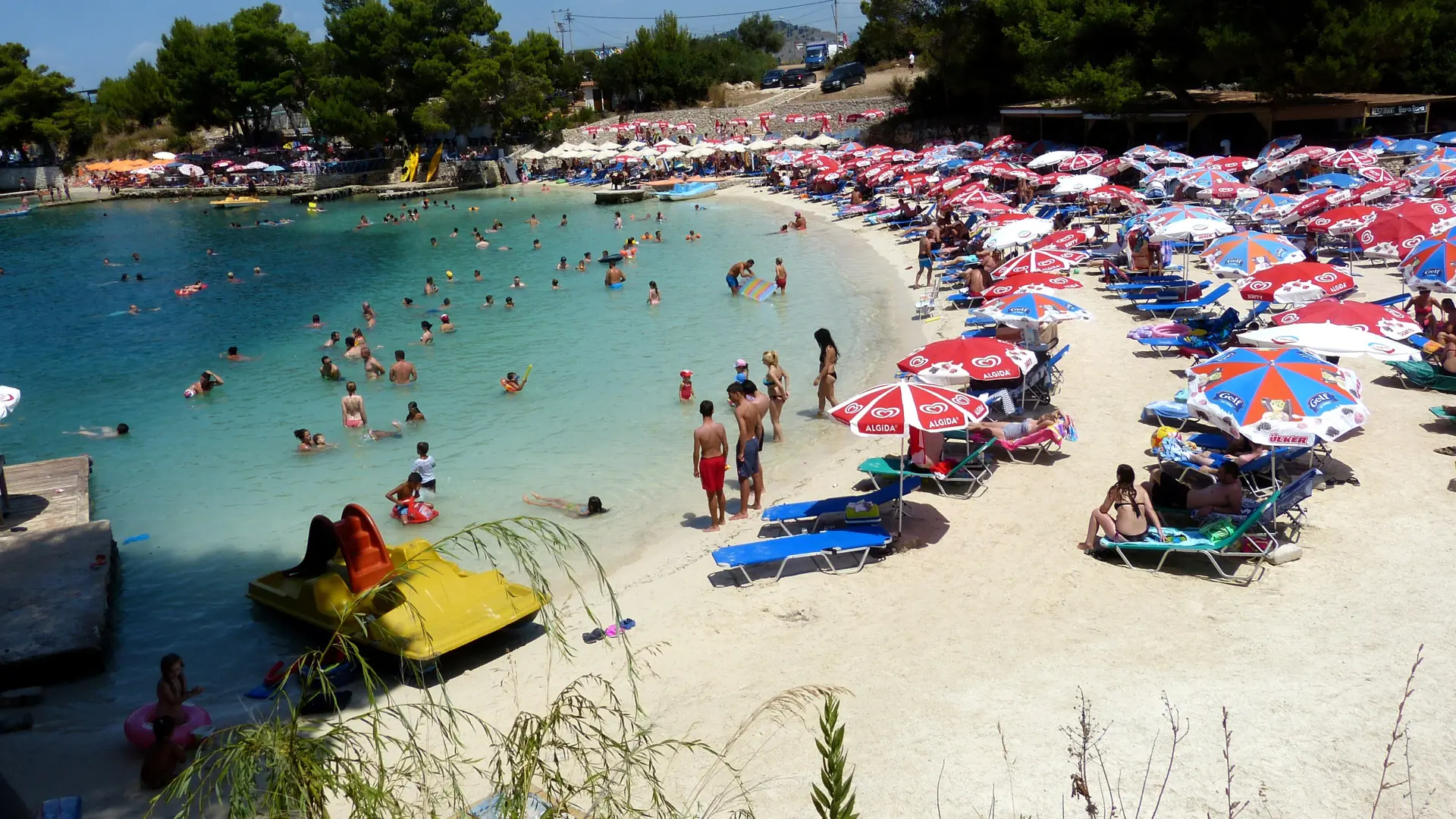 A sandy Ksamil cove lined with sunbeds and umbrellas beside shallow turquoise water on a summer day