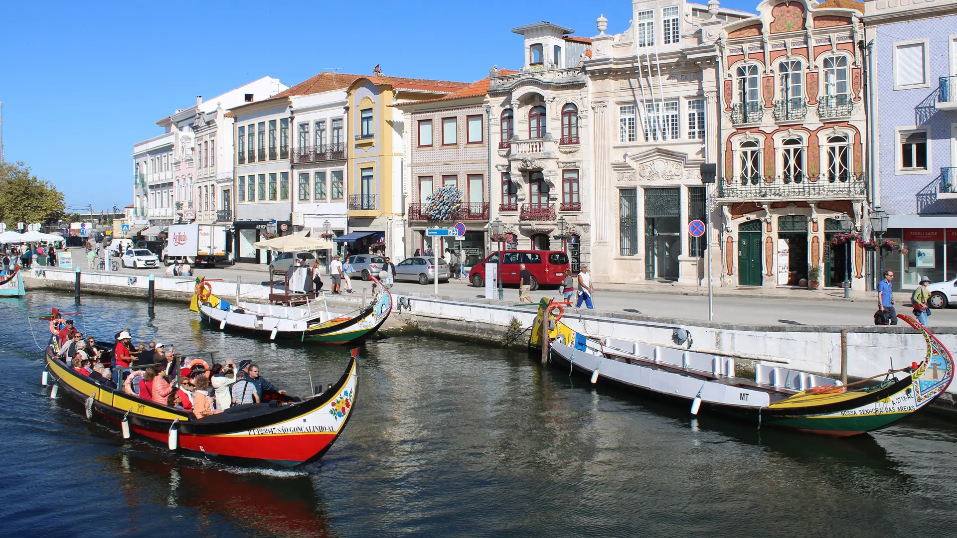 Colourful moliceiro boats passing Aveiro’s canal-side façades beneath a clear blue sky