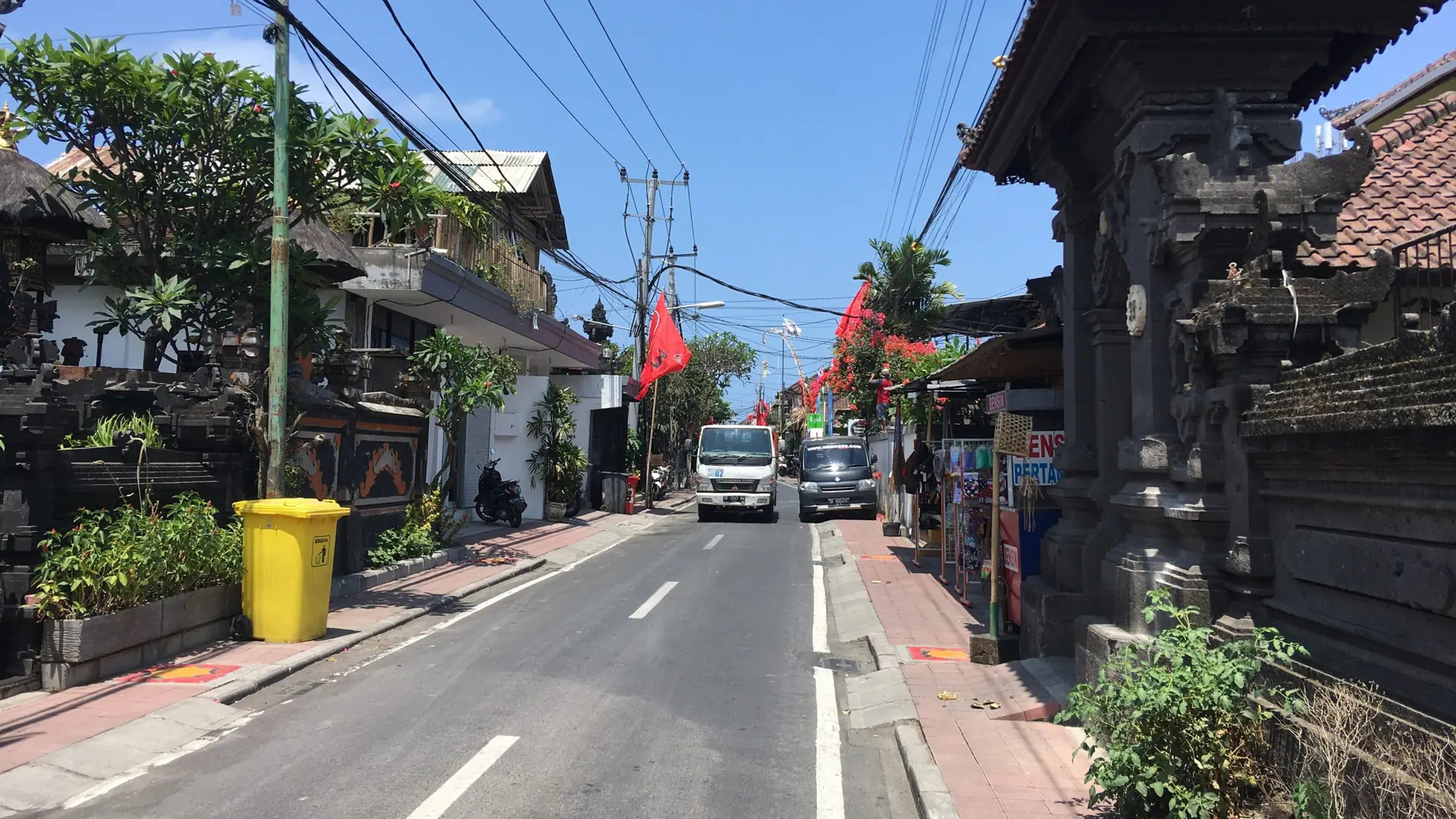 Red flags and a carved Balinese gateway beside a sunny Seminyak street