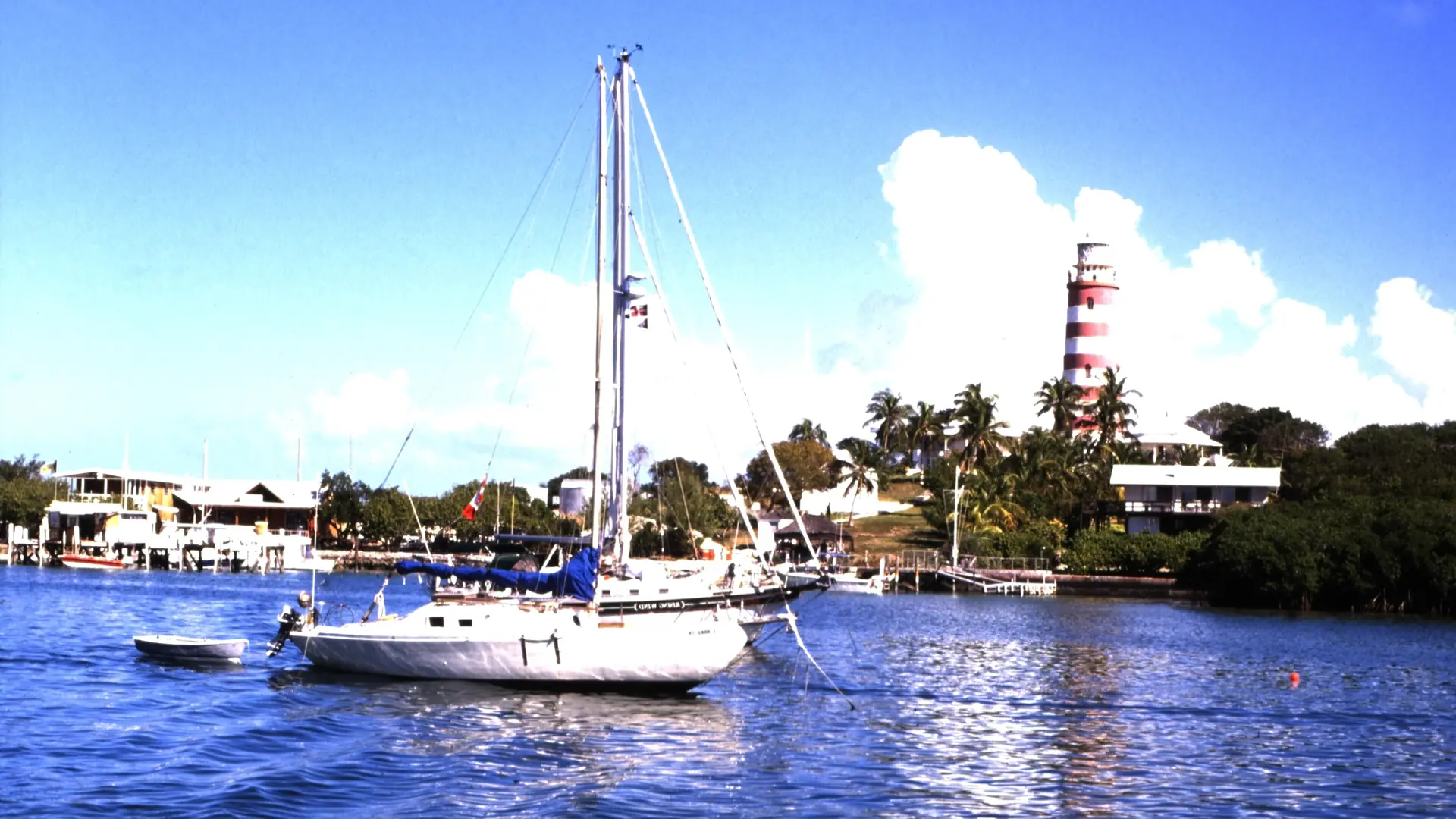 A yacht and the striped Elbow Reef lighthouse at Hope Town in the Abacos