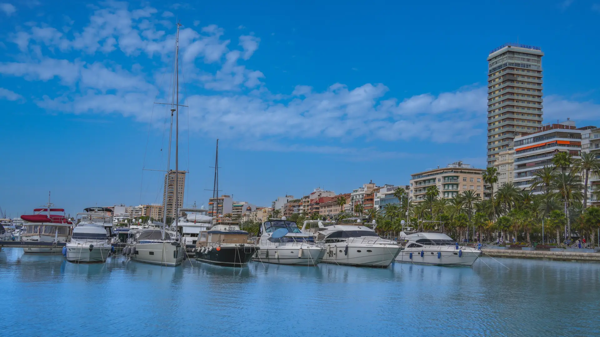 Yachts and reflections in Alicante marina, with Gran Sol on the waterfront skyline