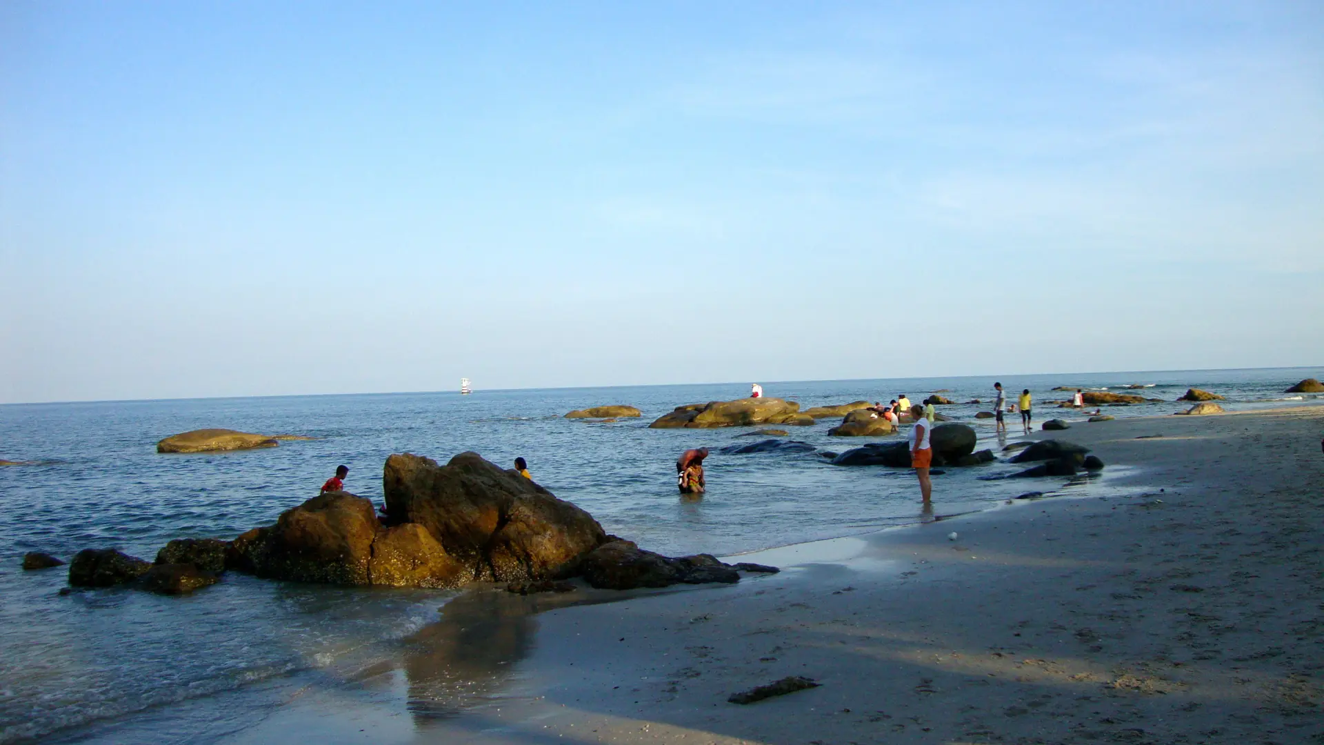Visitors beside sunlit rocks and the sea on Hua Hin Beach