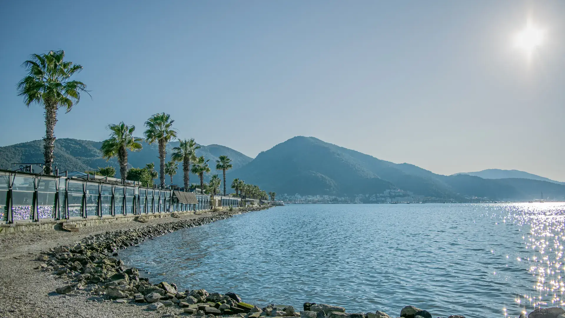 Sunny Fethiye Bay beach with palms, green mountains and bright Mediterranean water