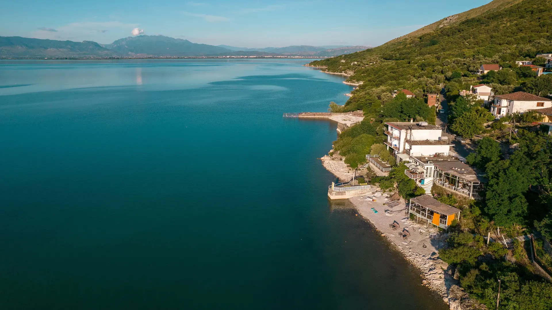 Houses on the shore at Zogaj above the clear water of Lake Shkodra on a sunny day
