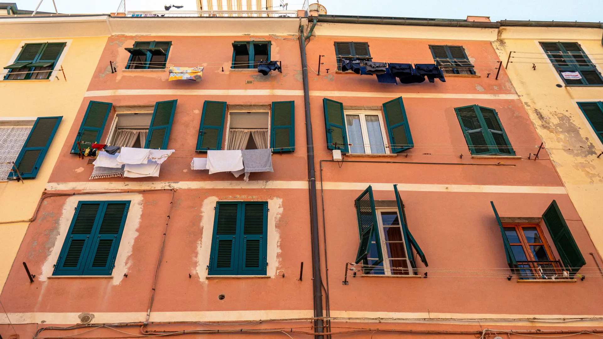 laundry hanging from green-shuttered windows on a warm terracotta facade in Naples