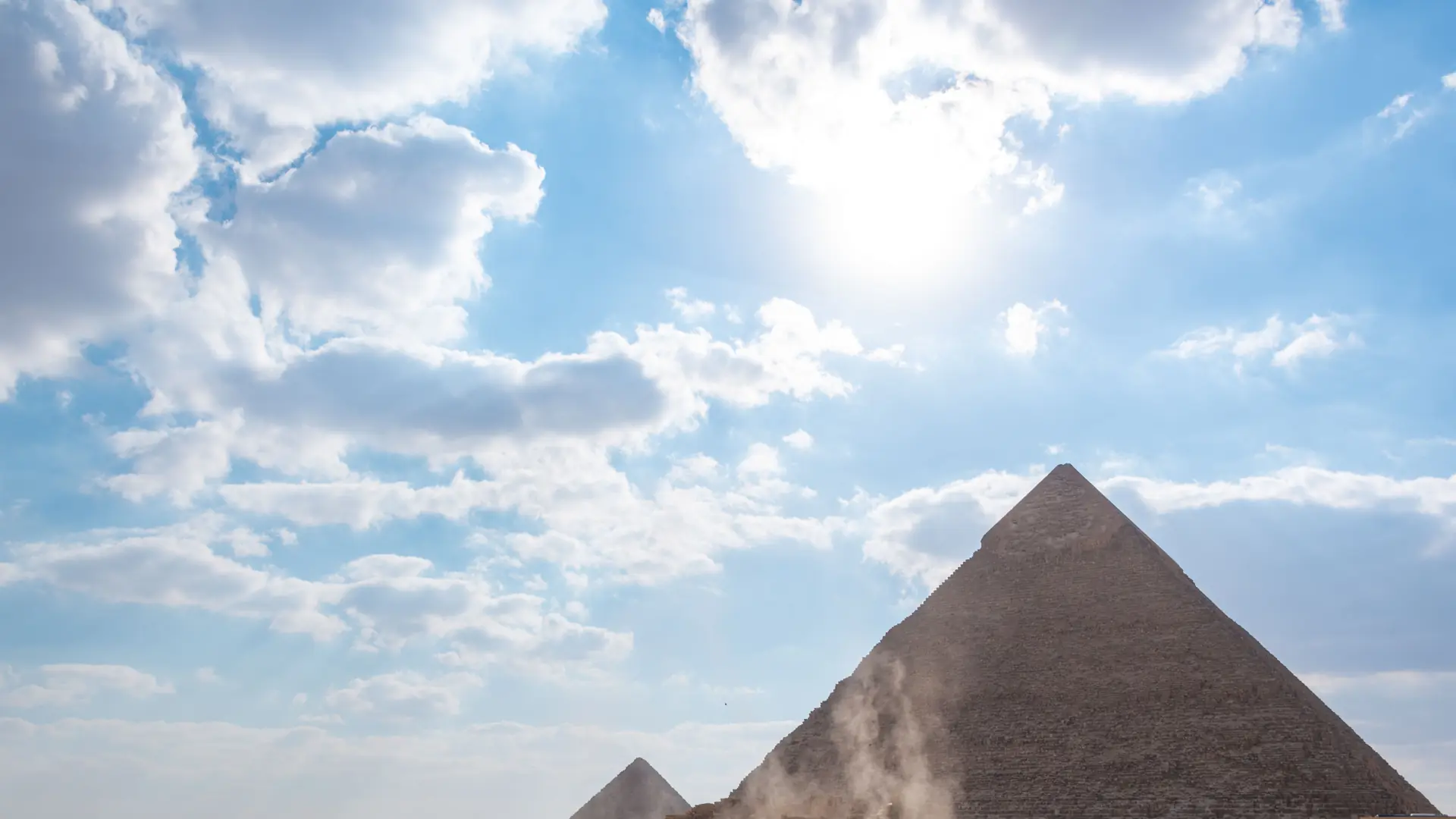 Sunlit Giza pyramid beneath a bright cloud-streaked sky