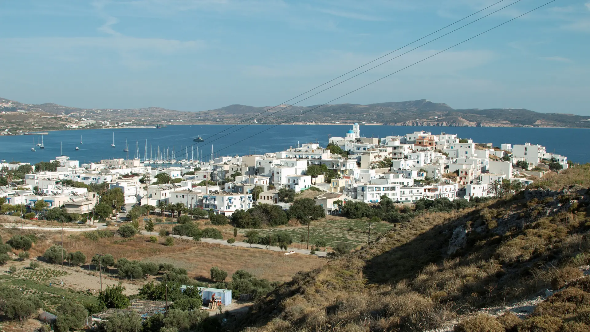 White buildings and the marina of Adamas above the gulf of Milos, seen from the hillside in daylight