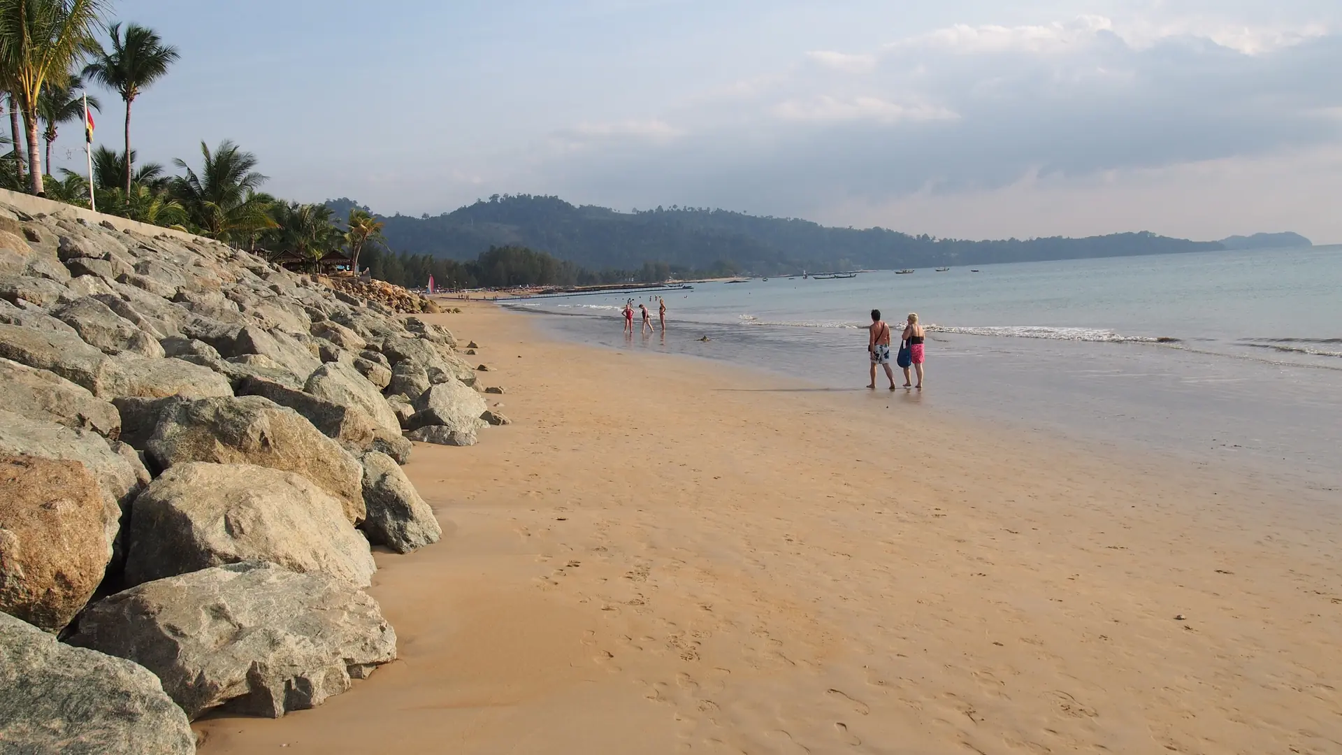 A broad Khao Lak beach edged by palms and low green hills