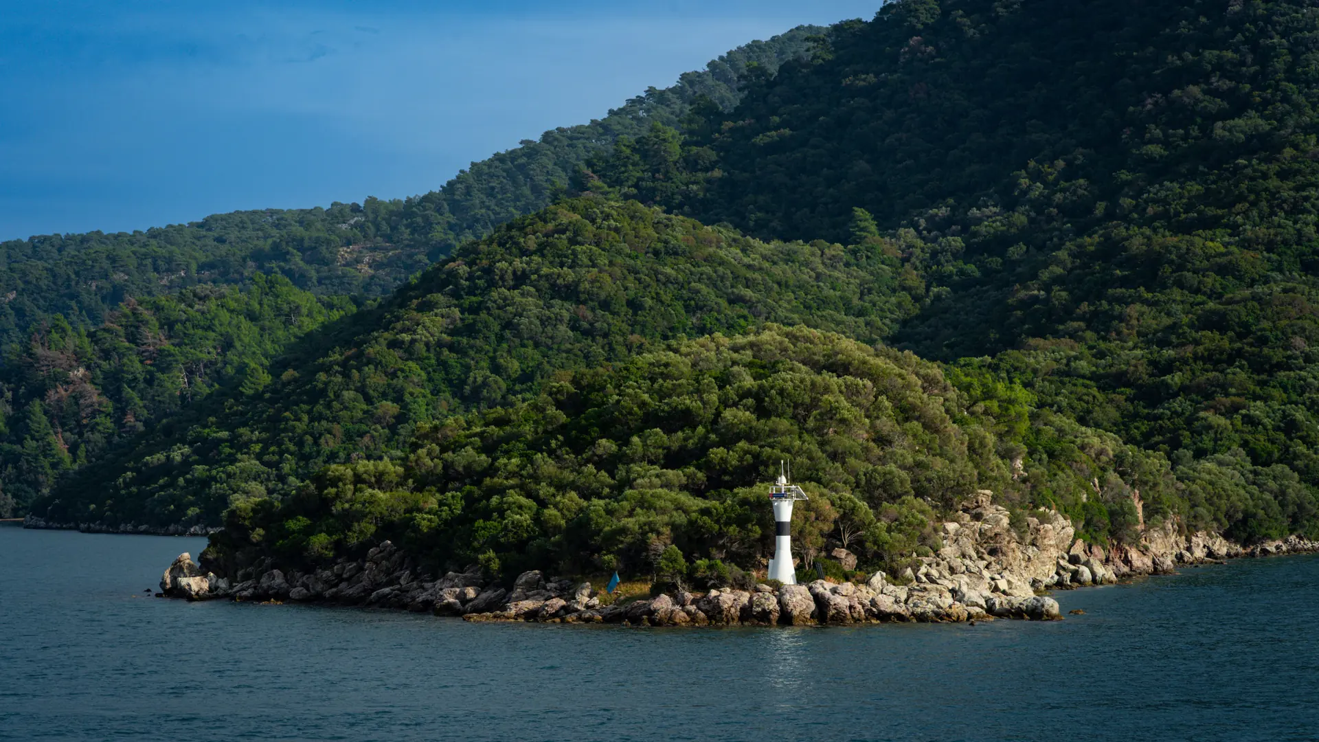 A lighthouse on a rocky islet beside the pine-covered Marmaris coastline