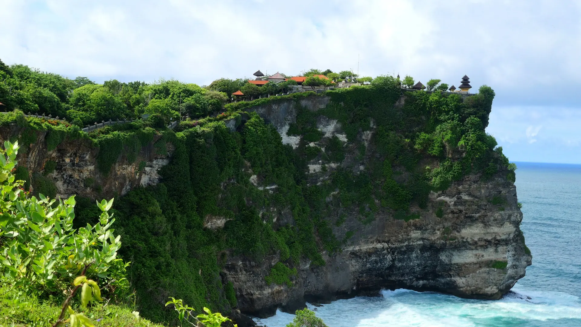 Pura Uluwatu temple on a green limestone promontory above turquoise surf along the wider western Uluwatu coast