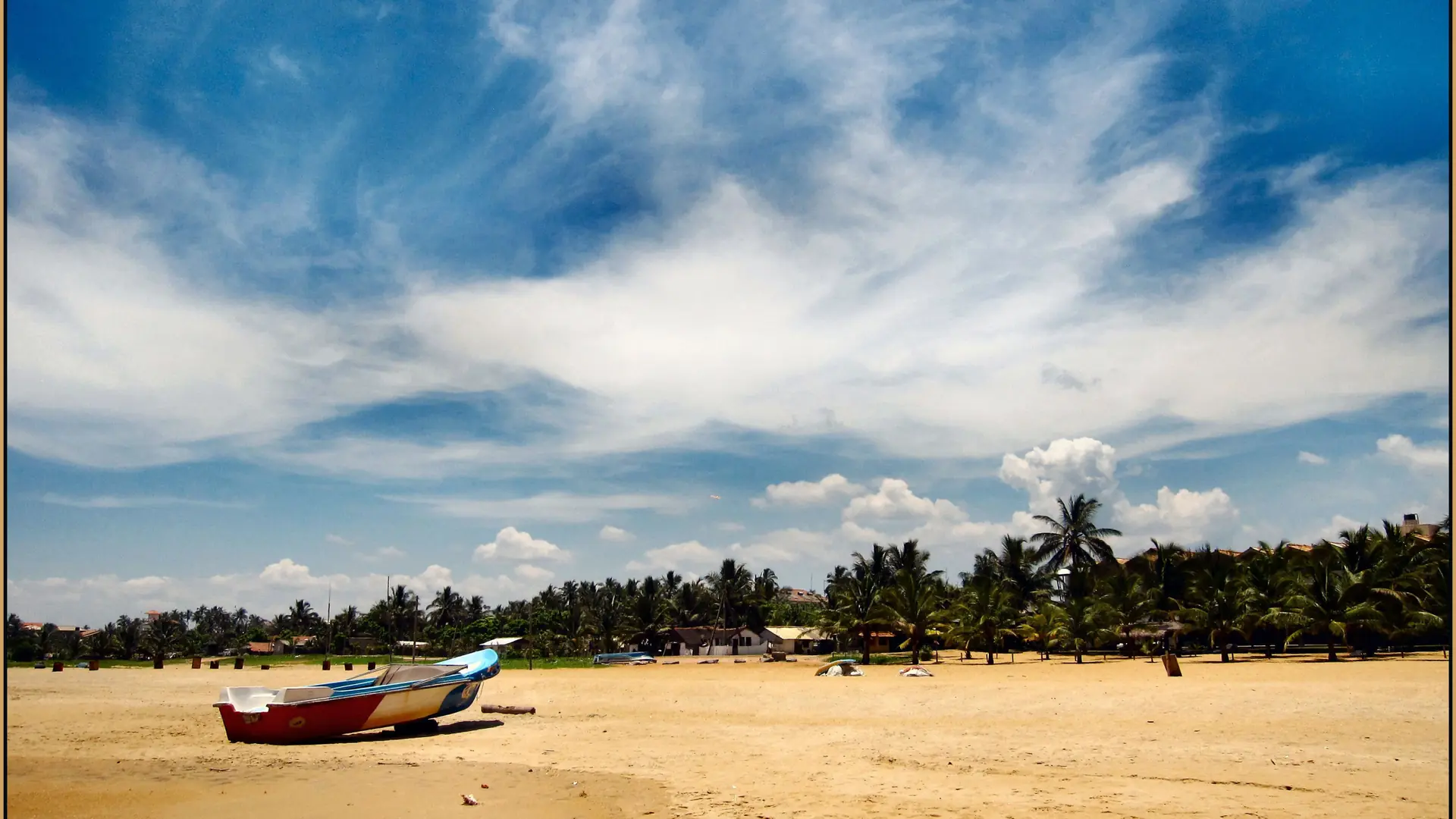 Fishing boat on the wide sandy Negombo beach beneath a blue sky