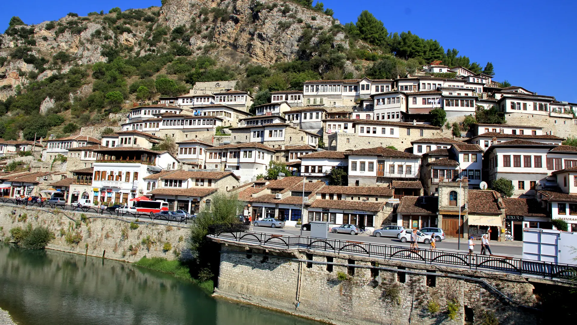 Tiers of white Ottoman houses in Mangalem rising above the Osum river wall under a clear blue sky