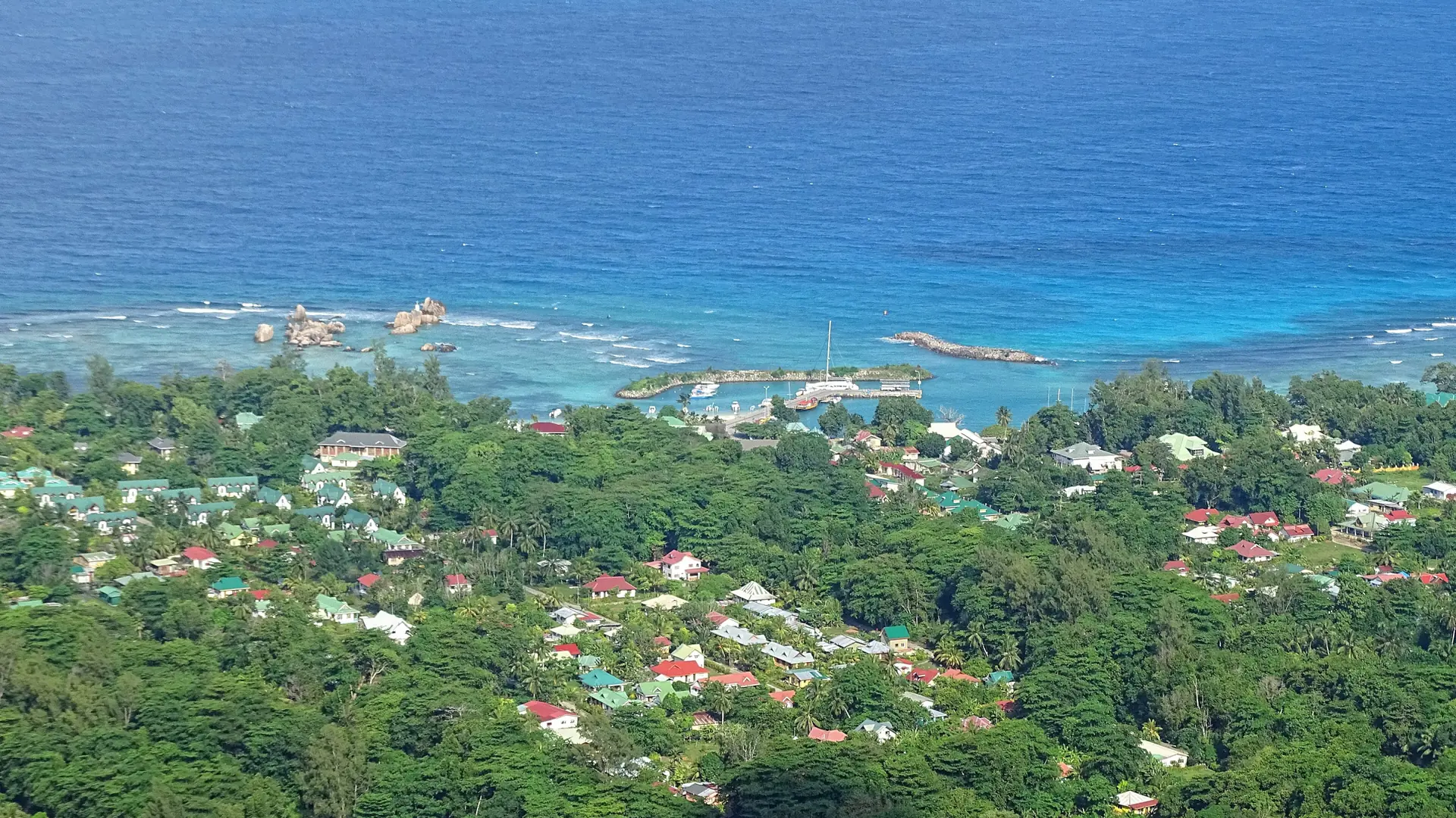Sunlit view over La Passe's green village and blue coast from above La Digue
