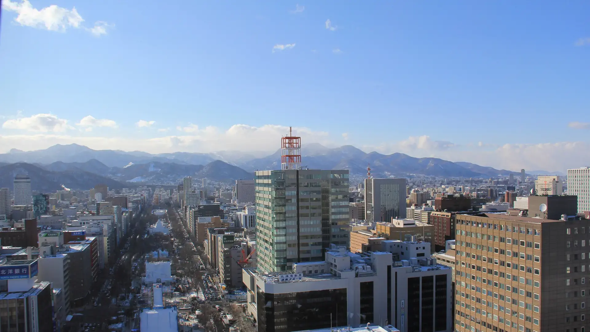 wide view across central Sapporo to snow-bright mountains beneath a clear blue sky