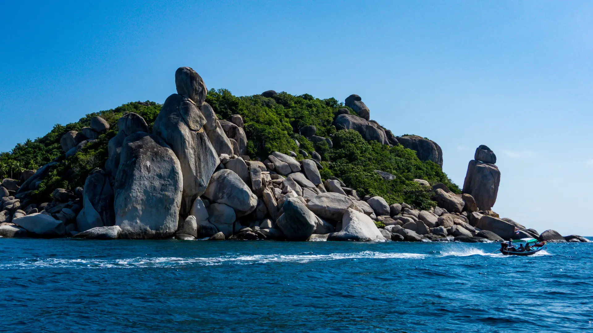 A rocky islet and a boat in blue water off Koh Tao, a wider view rather than Mae Haad
