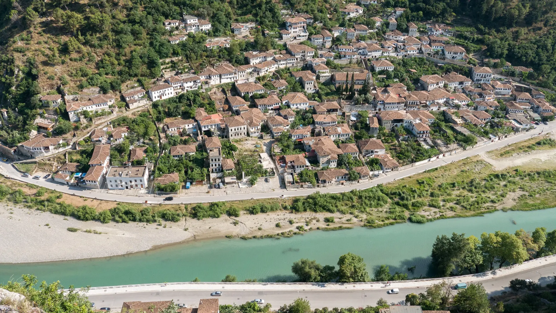 The old houses of Berat climbing above the green Osum river, seen from the castle hill in sunshine