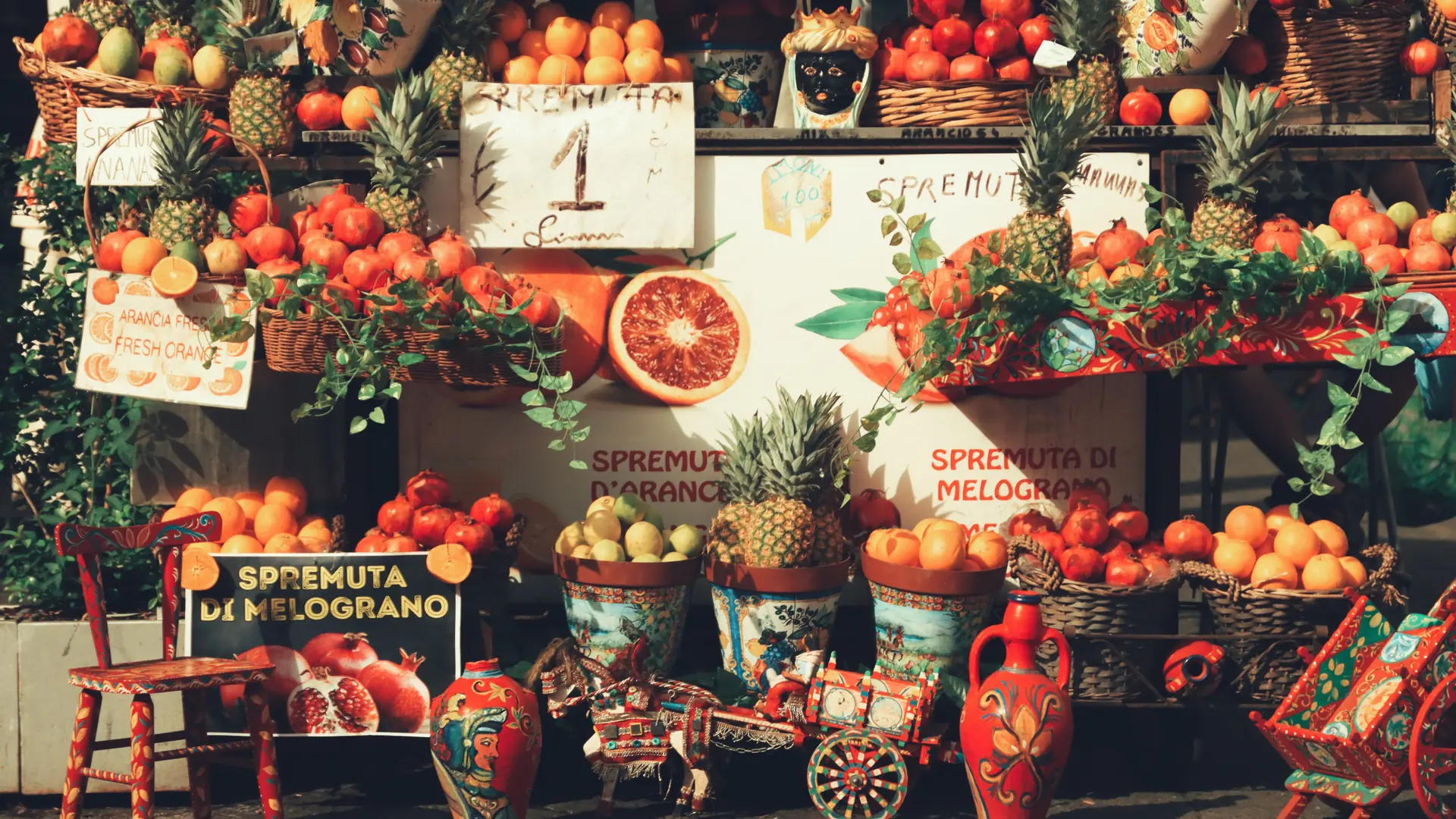 A sunlit Sicilian fruit stall piled with oranges and pomegranates for fresh-pressed spremuta juice