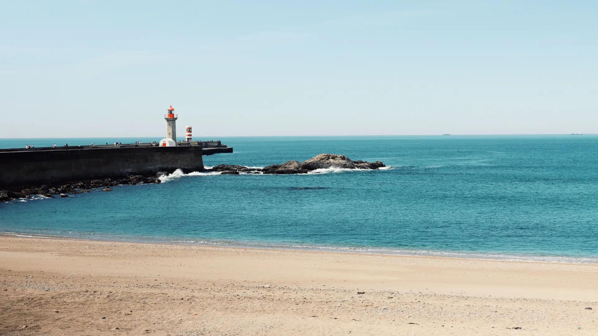 Felgueiras lighthouse and a sandy beach beside turquoise Atlantic water at Foz do Douro in Porto