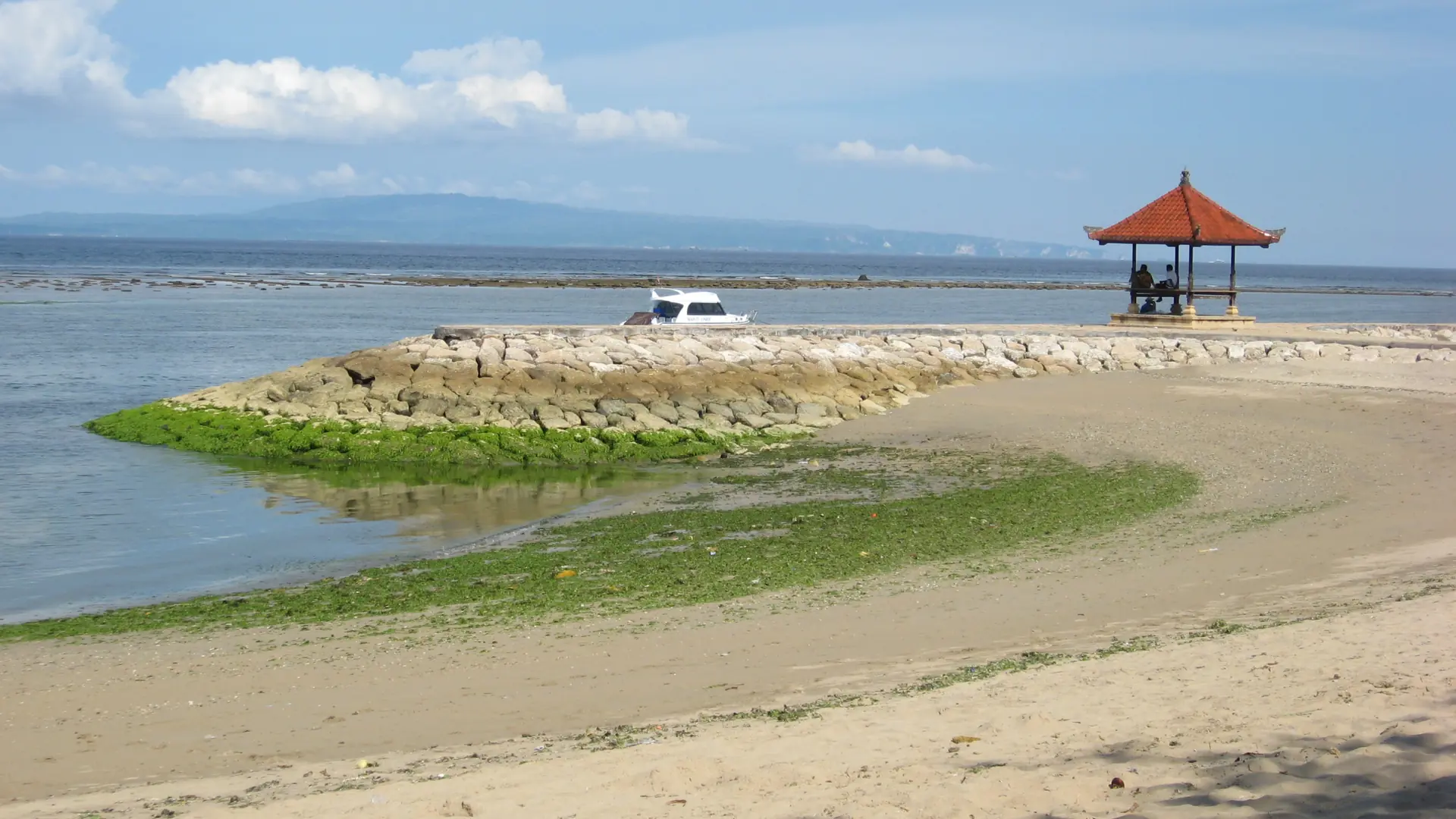 Red-roofed seaside pavilion and green tidal shore at Sanur Beach