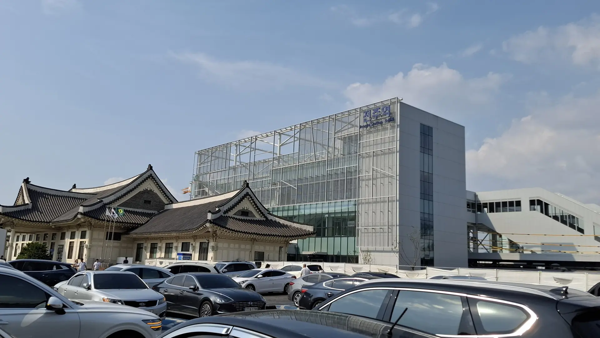 Jeonju Station's hanok-inspired tiled-roof exterior beside its modern glass concourse, in bright daylight