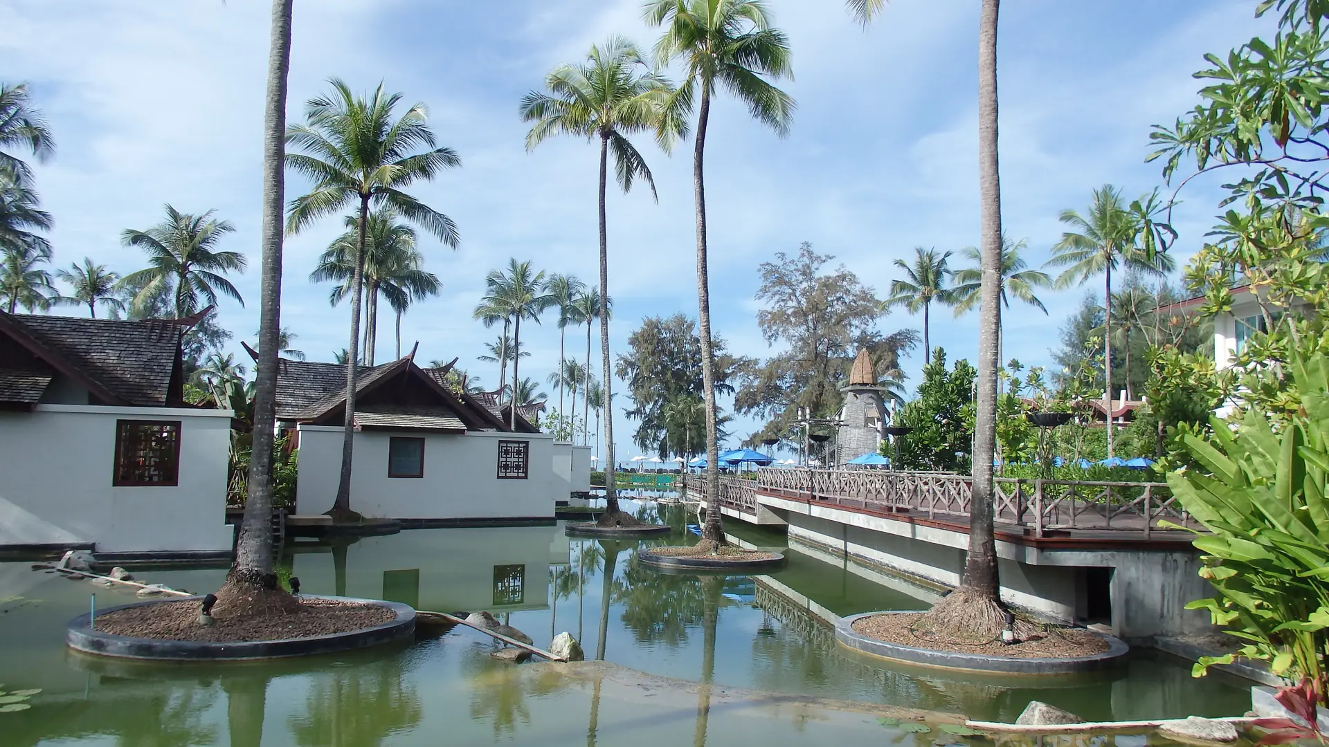 Sunlit palms, waterside buildings and a garden bridge at Bang Muang in wider Khao Lak