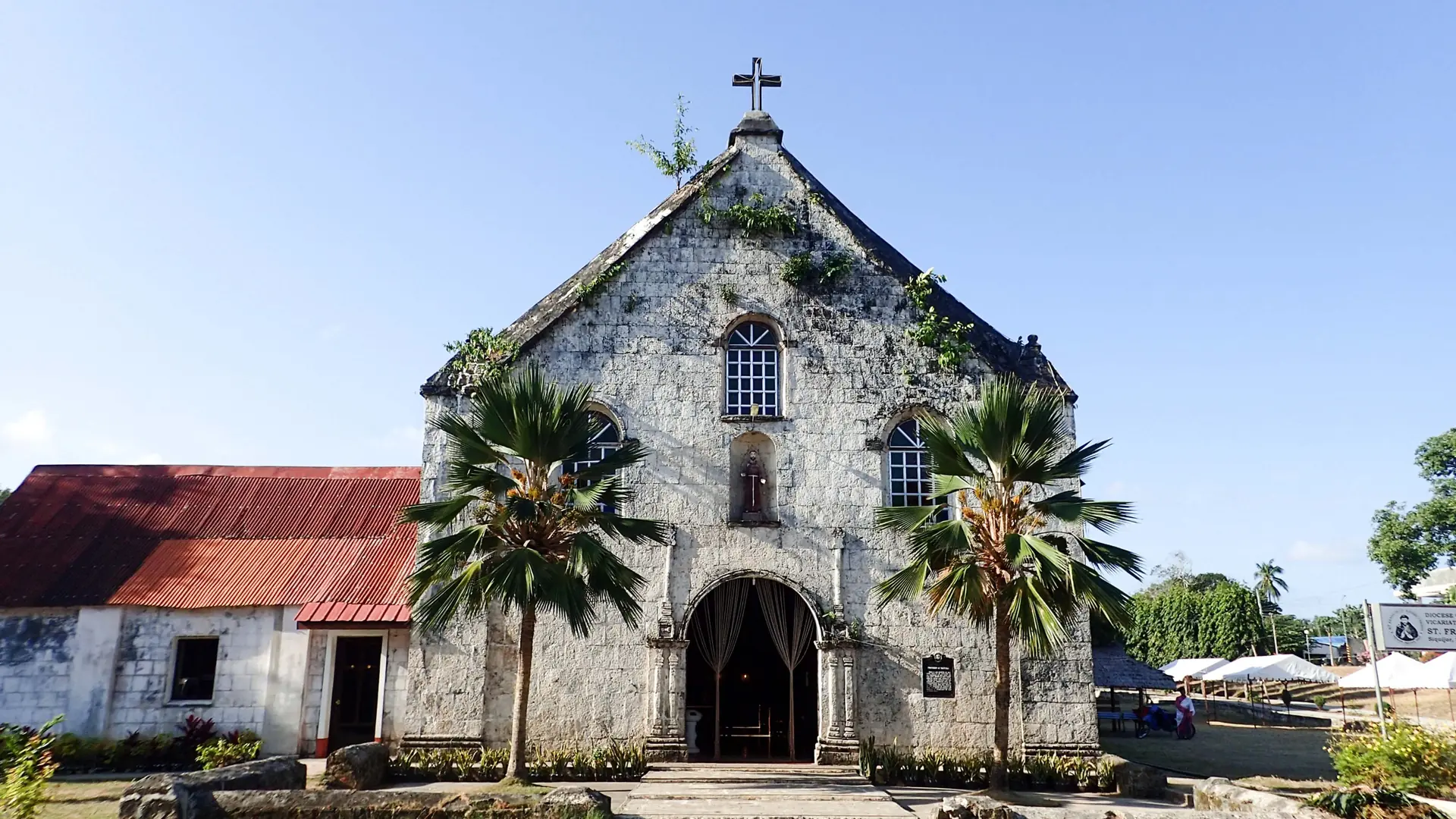 Sunlit stone facade and complete roof cross of St Francis of Assisi Church in Siquijor town