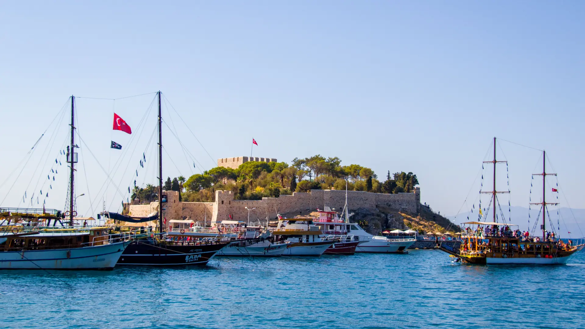 Daylit Pigeon Island castle with traditional excursion boats on the Kuşadası waterfront
