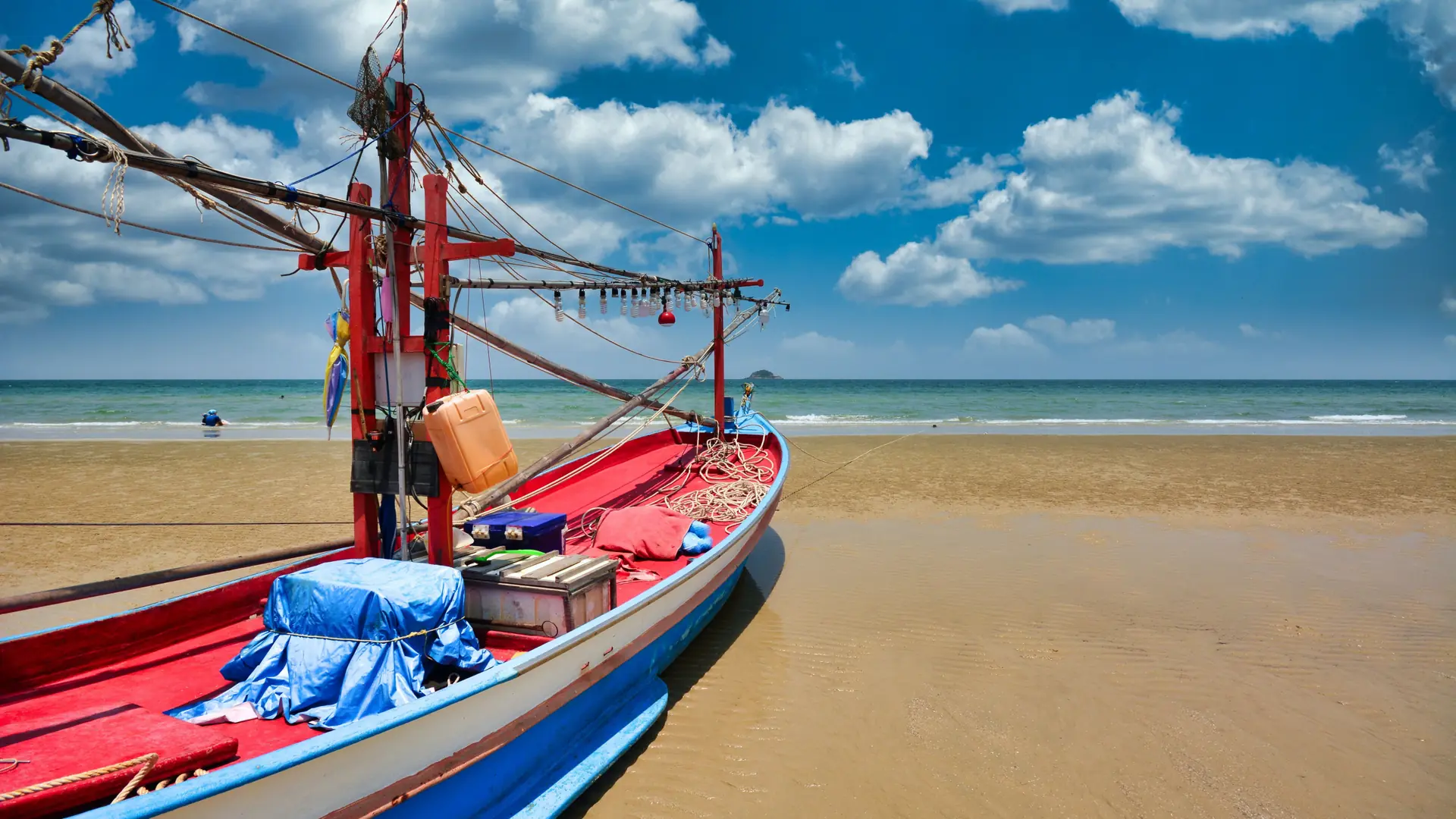 A red and blue fishing boat on sunlit Hua Hin sand, a wider coastal scene rather than Pranburi