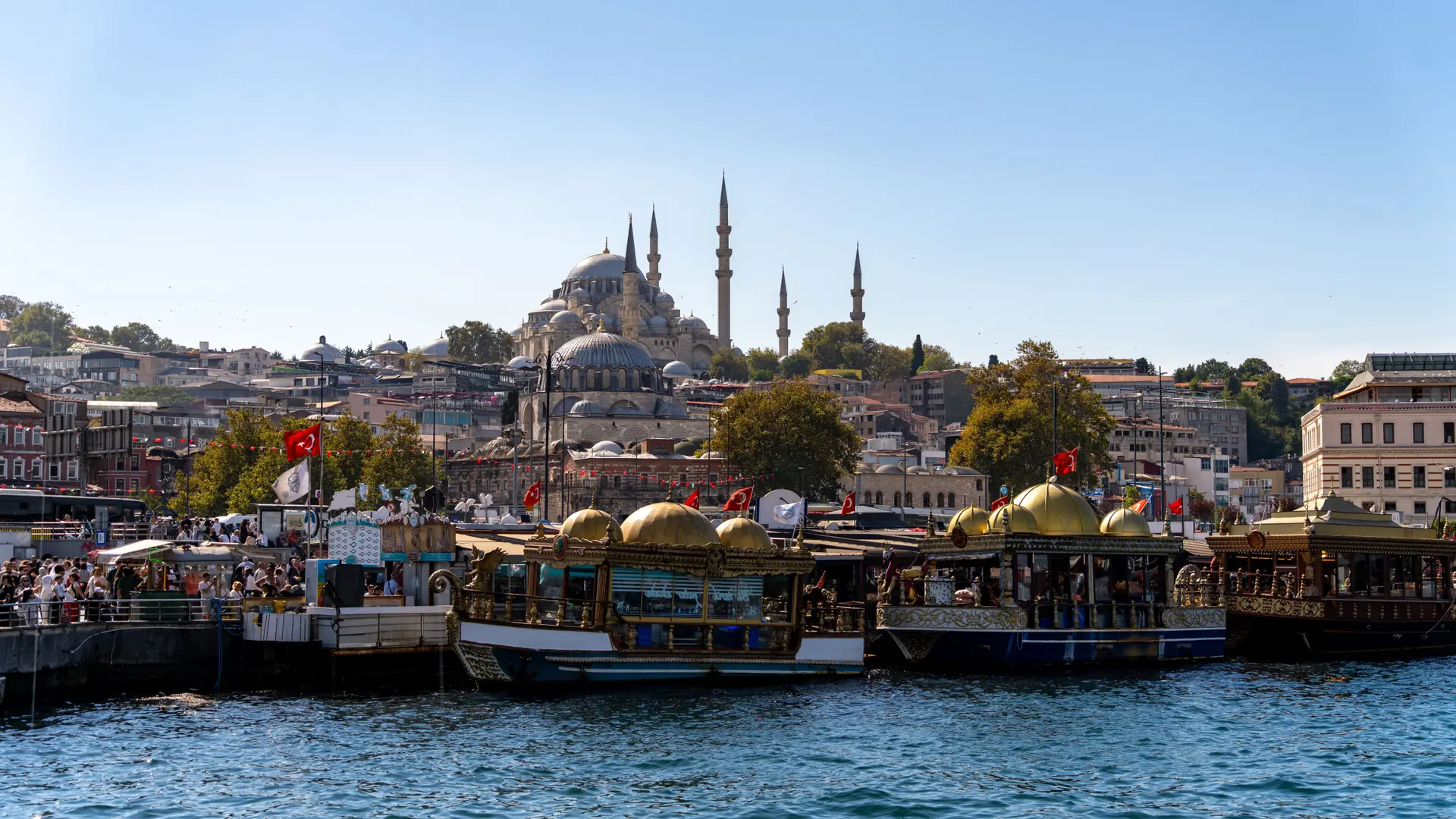 Decorated boats along Eminönü’s waterfront beneath Istanbul’s mosque skyline in bright daylight