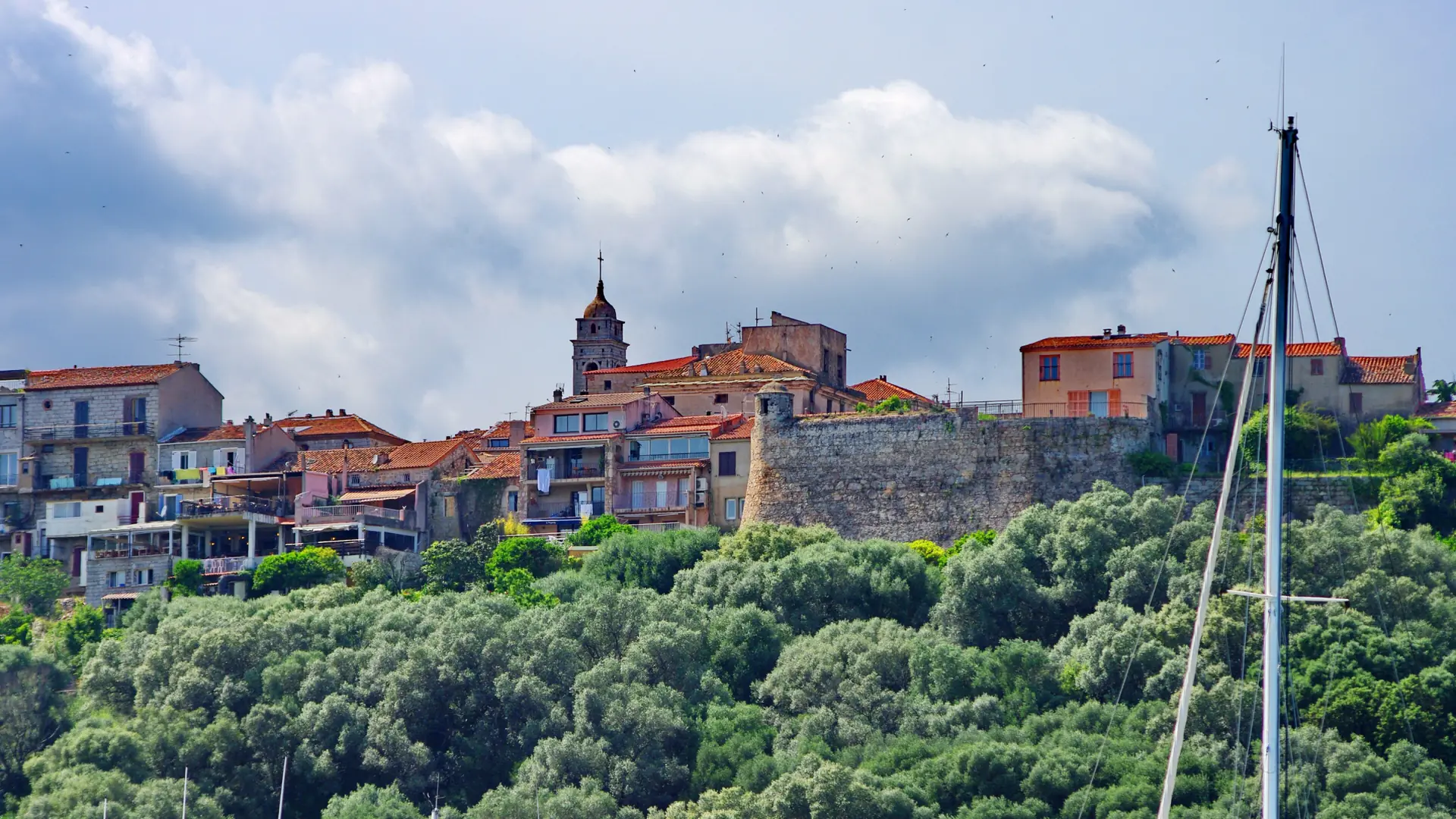 Porto-Vecchio’s stone citadel walls and red-roofed old town above a green slope, with the church bell tower beyond