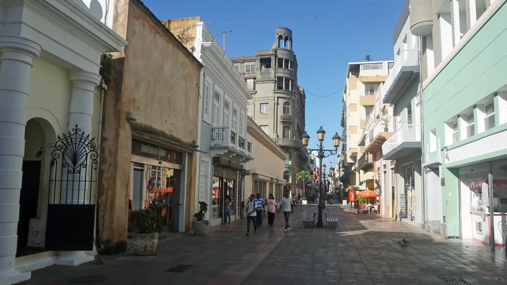 Sunlit Calle El Conde street with colonial buildings and a church tower in Santo Domingo
