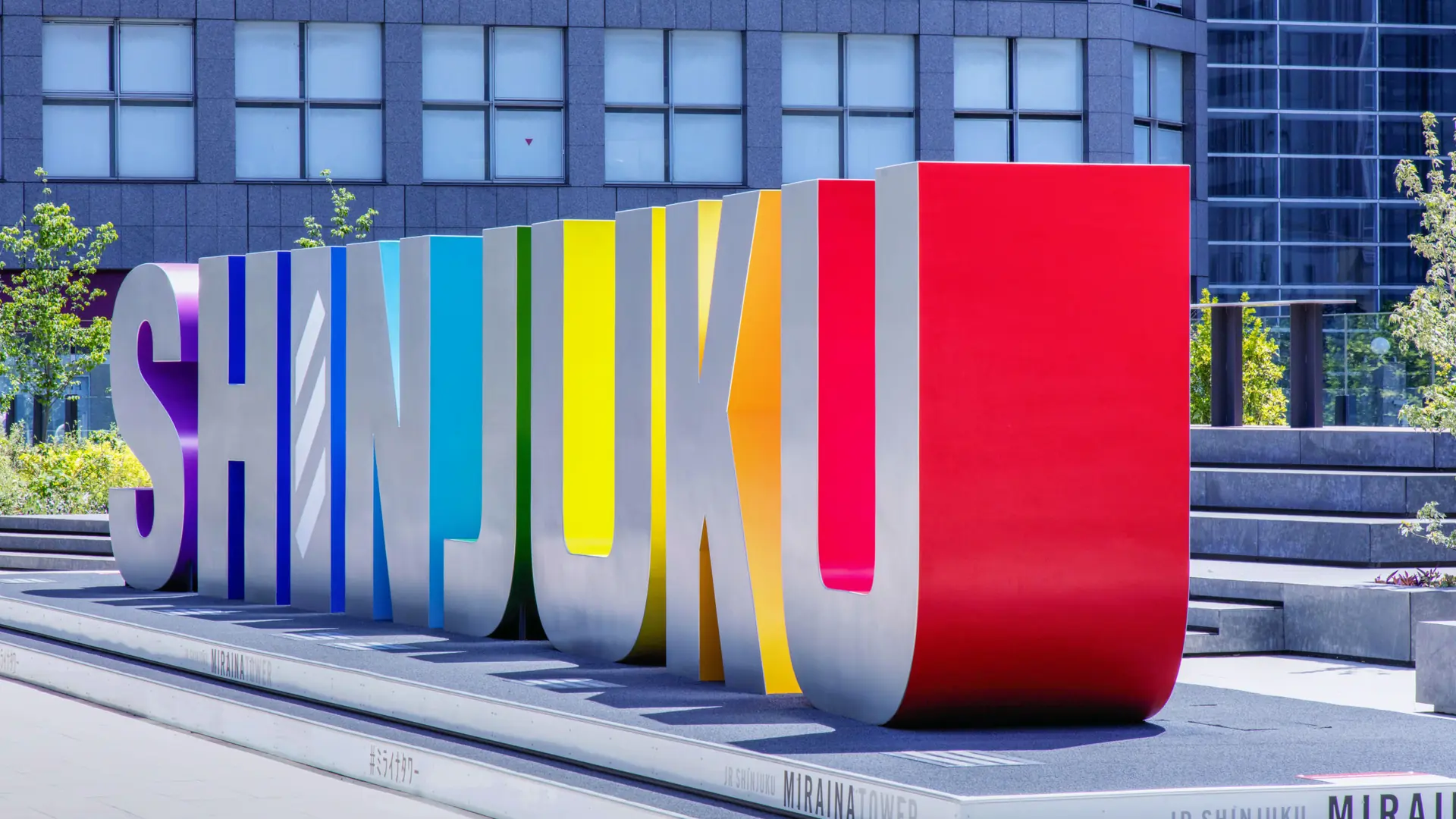 Colourful SHINJUKU letters outside JR Shinjuku Miraina Tower in bright daylight.