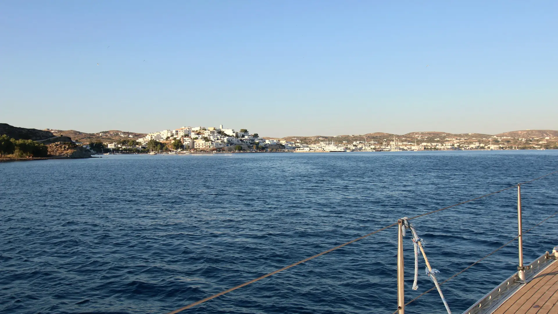 Adamas port town across blue water on Milos, viewed from a boat