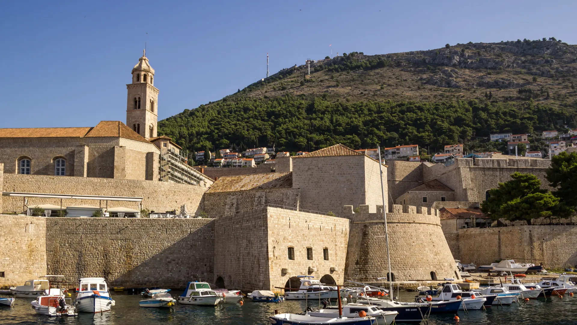 Fishing boats moored in Dubrovnik's Old Port below the city walls and bell tower