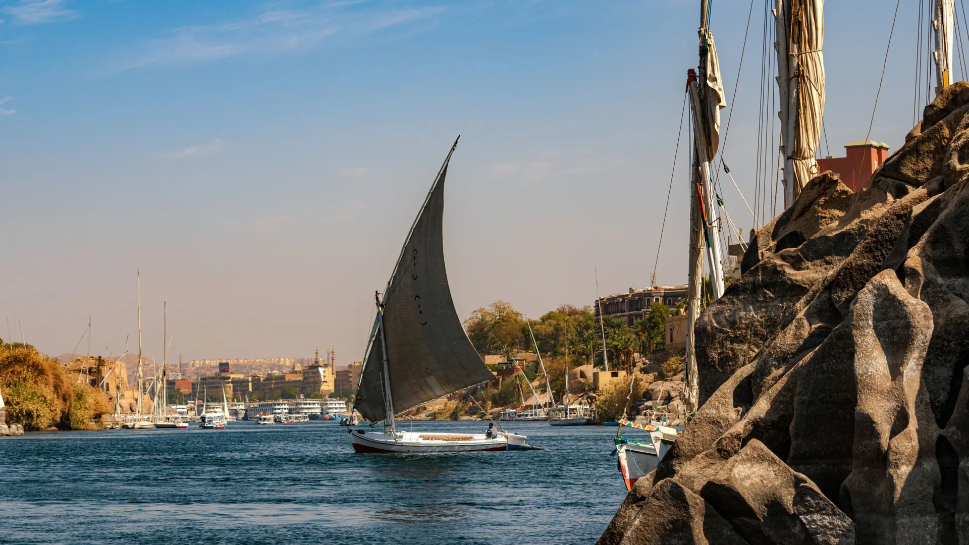 Sunlit felucca sailing beside granite rocks on the Nile at Aswan
