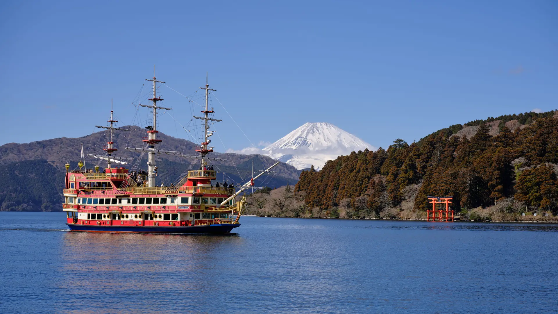 A red sightseeing boat on Lake Ashi with Mount Fuji and Hakone Shrine’s waterfront torii
