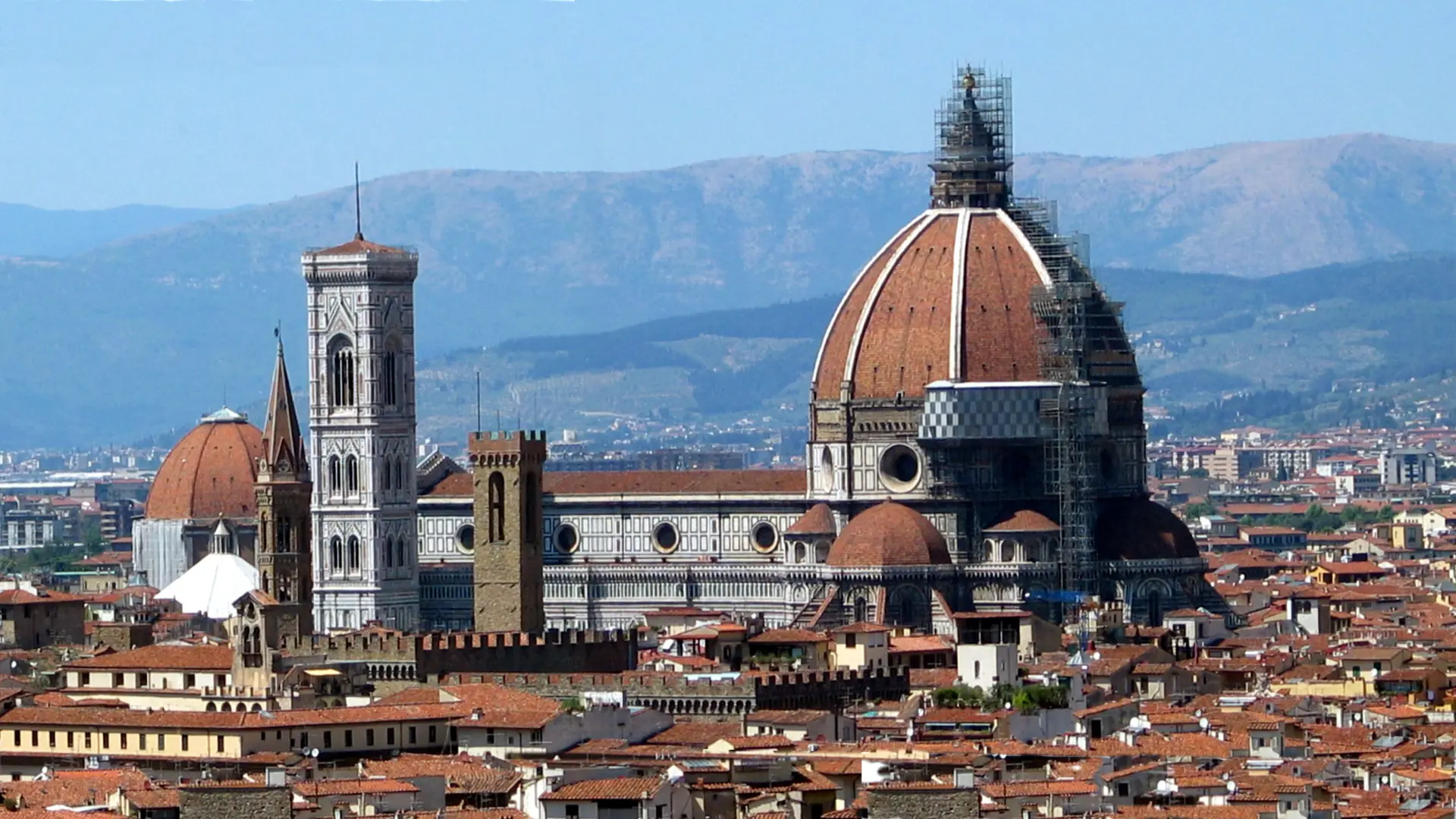 sunlit view of Florence Duomo dome above terracotta roofs and historic stone streets