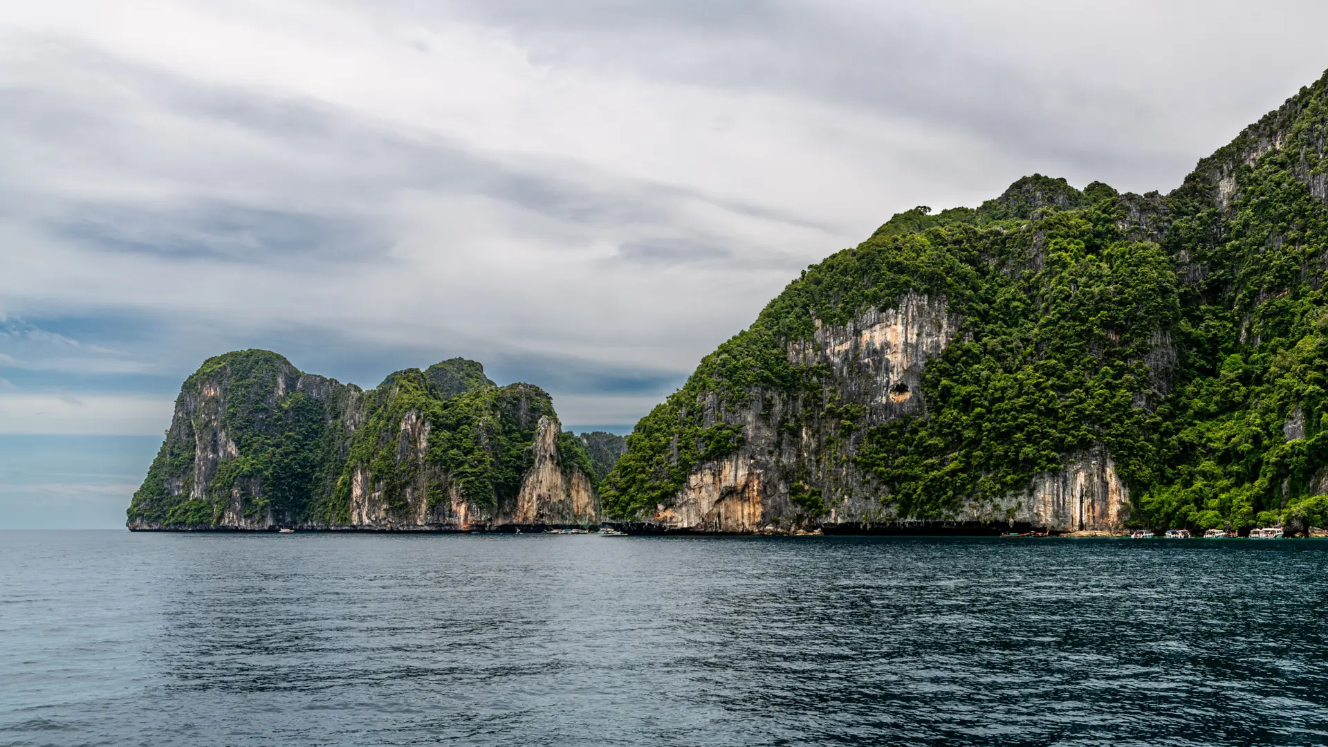 Green limestone cliffs dropping into calm blue water along Phuket's coast