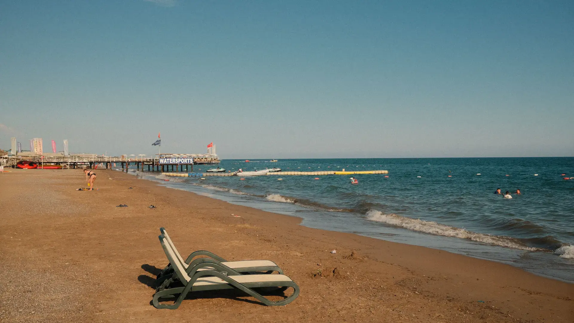 Bright Antalya coast beach with sun loungers, a long pier and clear blue water