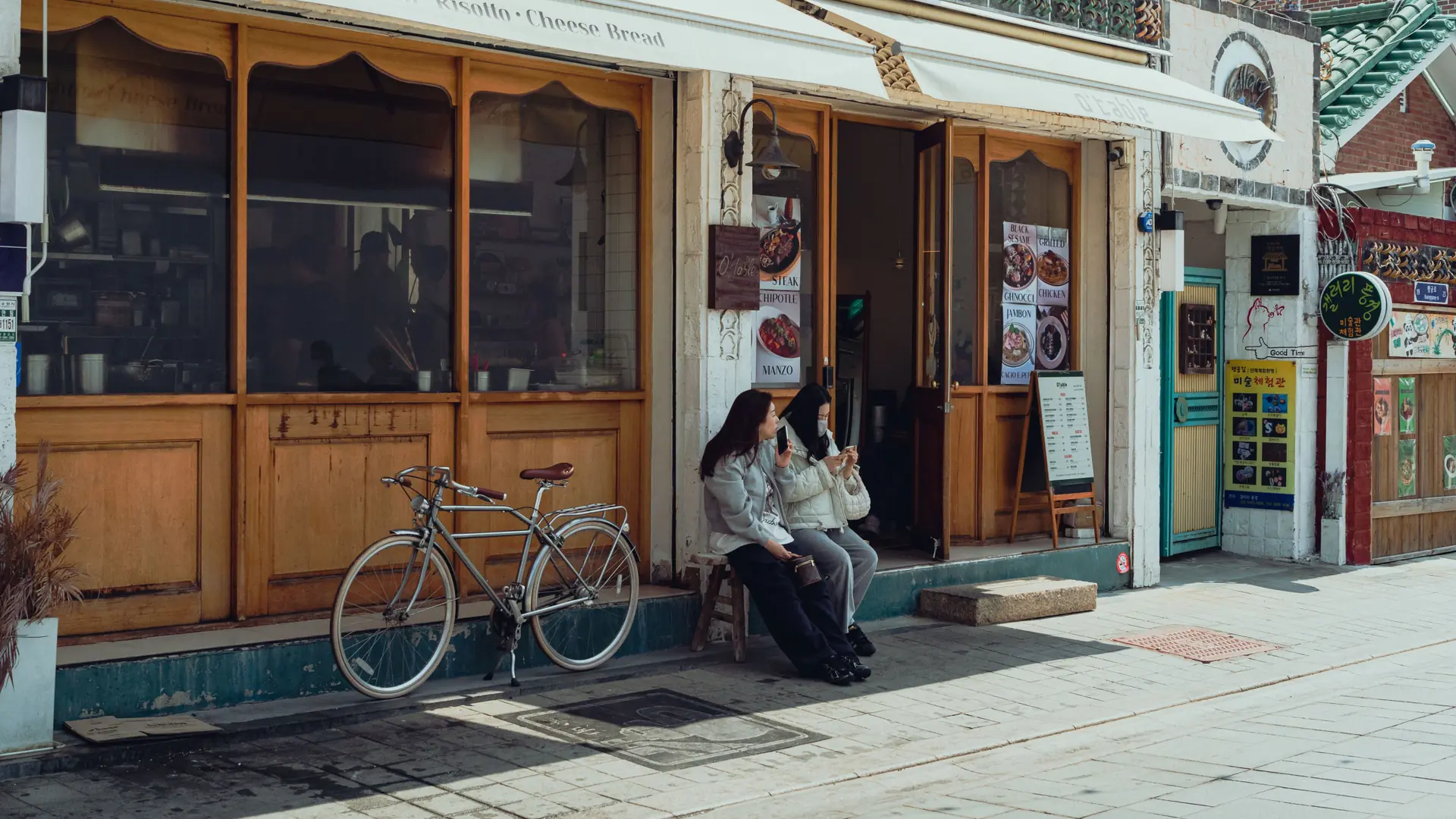 A Western-style cafe storefront in a narrow hanok-adjacent Seoul alley, with signage and a bicycle parked outside in bright daylight